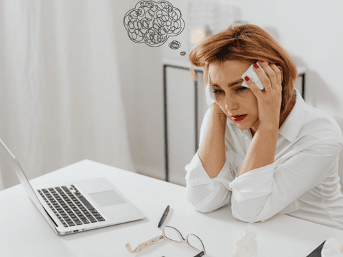 Mulher com expressão de cansaço, segurando a cabeça diante de um computador, com balão de pensamento indicando preocupação. Mulher com expressão de cansaço, segurando a cabeça diante de um computador, com balão de pensamento indicando preocupação.