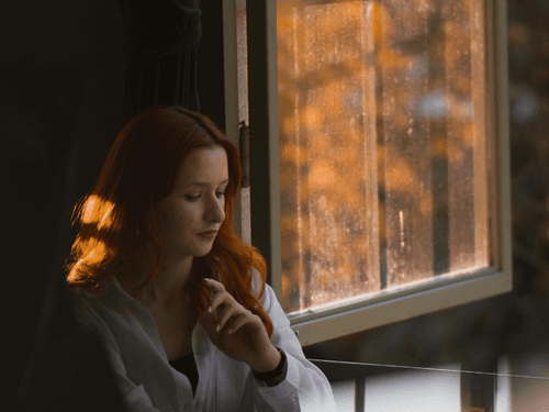 Mulher sentada ao lado de uma janela, iluminada pela luz natural, em postura contemplativa. Mulher sentada ao lado de uma janela, iluminada pela luz natural, em postura contemplativa.