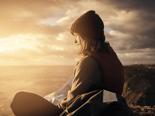 Mulher sentada em um penhasco à beira-mar, olhando o horizonte ao pôr do sol. Mulher sentada em um penhasco à beira-mar, olhando o horizonte ao pôr do sol.